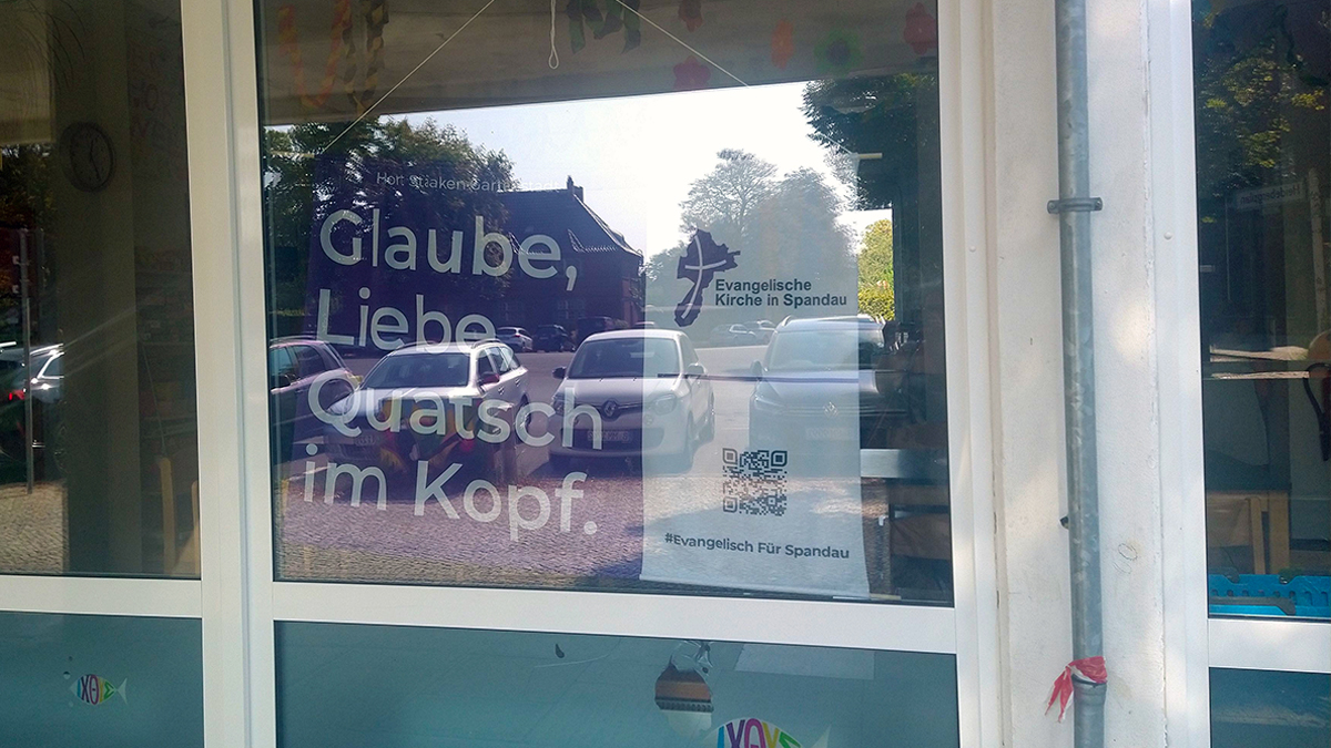 Lila Banner im Schaufenster: Glaube, Liebe, Quatsch im Kopf.