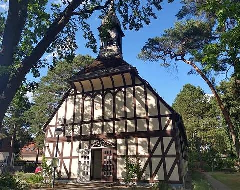 Eine Fachwerkkirche mit einem Turm über dem Eingang, umgeben von Bäumen.