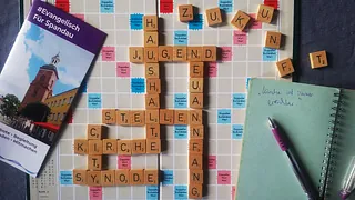 Symbolbild: Kirchenkreisbroschüre mit Scrabble-Bord mit Begriffen wie Synode, Haushalte, Kirche