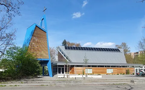 Jeremiakirche mit freistehendem Glockenturm, holzverkleidetem Erdgeschoß und Pultdach mit Solarzellen