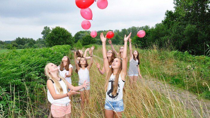 Mädchen stehen im hohen Gras und lassen Luftballons fliegen