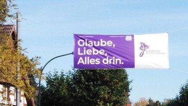 Über die Straße ist ein Banner gespannt: Glaube, Liebe, Alles drin
