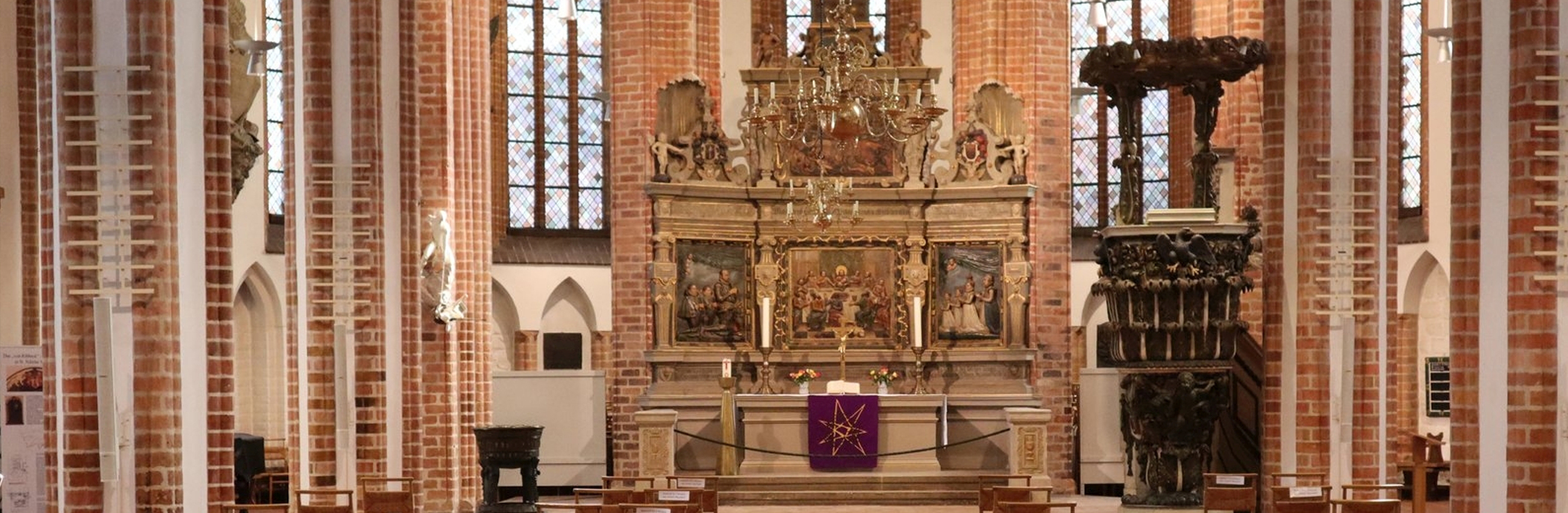 Altarraum der St. Nikolaikirche mit barockem Altar und Kanzel und weißen Pfeilern mit Backsteinrippen