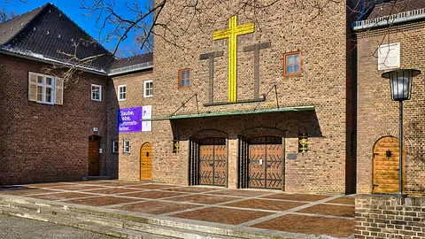 Vorplatz Christophoruskirche, schlichte Backsteingebäude mit großem goldenen Kreuz über dem Doppel-Portal