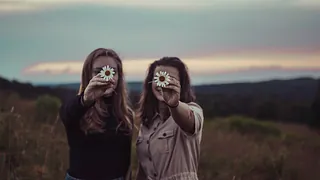 Symbolbild: Zwei Frauen halten eine Blüte vor ihr Gesicht